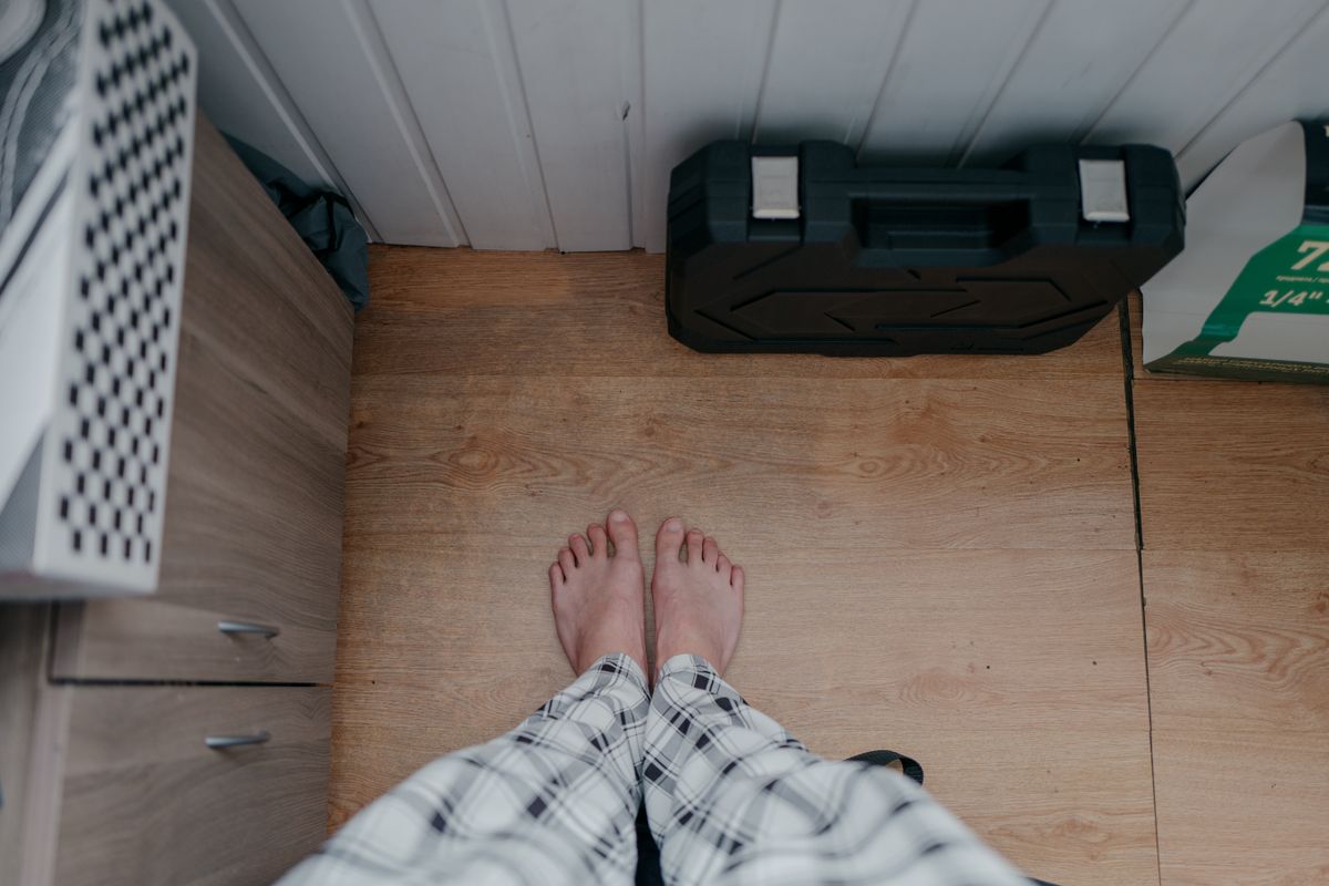 Overhead view of bare feet in pajamas on wooden floor indoors with tool box nearby.