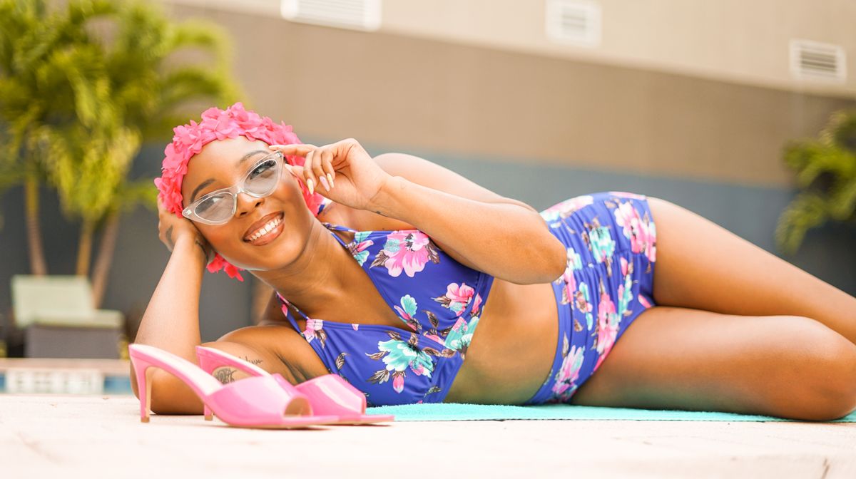 Smiling woman in floral swimsuit poses by the pool, showcasing summer style.