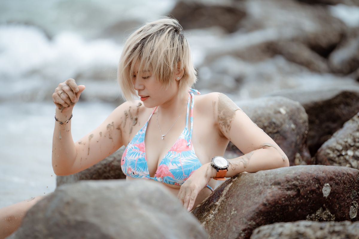 Woman in a floral bikini relaxing on a rocky beach, enjoying the summer vibes.
