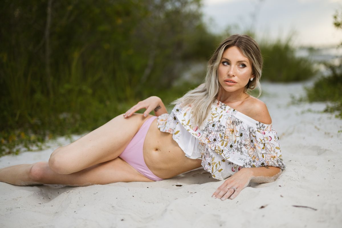 A fashionable woman posing in a floral crop top and pink bikini on a sandy beach.