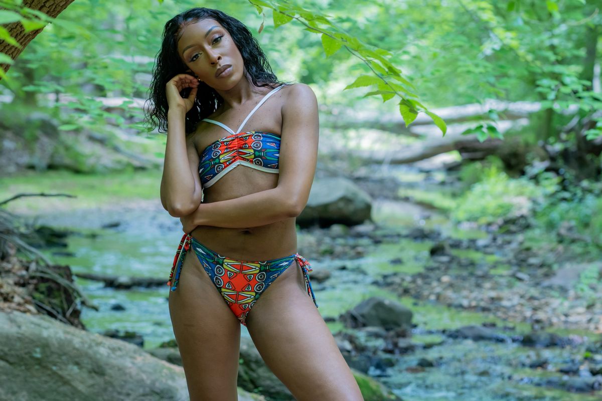 A woman in a colorful bikini poses by a scenic creek in a woodland setting, capturing the essence of summer.
