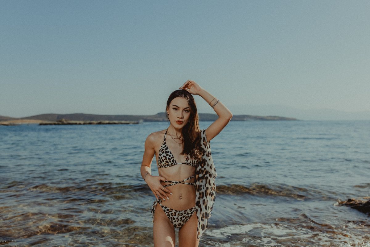 A young woman in a bikini stands by the sea on a sunny summer day, enjoying the warm beach environment.