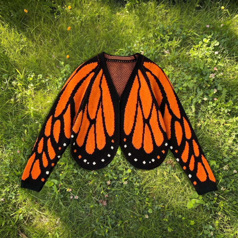 The monarch butterfly wing knit cardigan laid flat on grass, wings spread