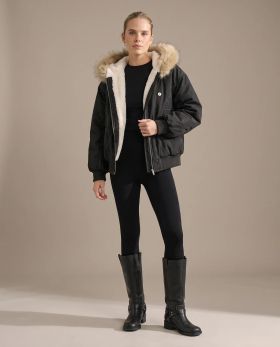 Full-length shot of the black faux fur lined bomber jacket worn open over black leggings and knee boots