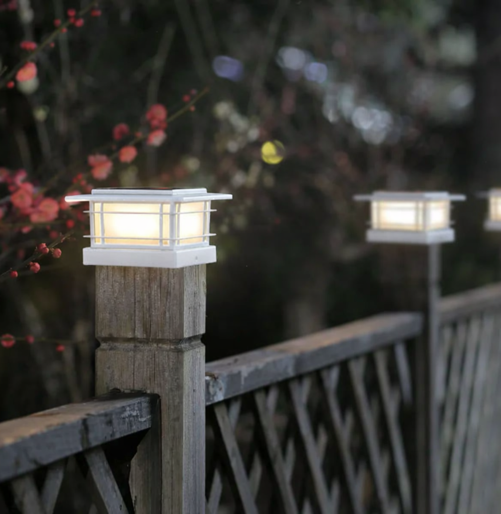 Solar post cap lights glowing warm white on a fence at dusk